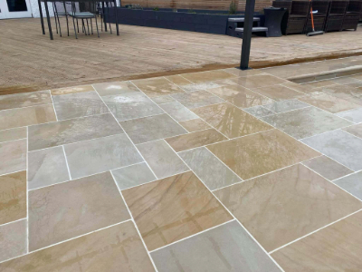 An outdoor area is fitted with professional, shiny paving tiles in a range of beige and brown shades. The tiles are cut into various rectangular shapes, arranged in a pattern that suggests meticulous planning and installation.