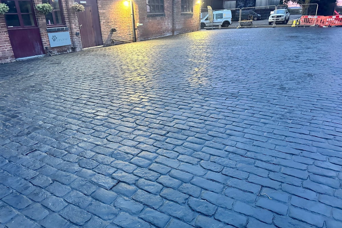 The image shows a driveway paved with blue cobblestones which gives it a classic and professional look. The cobblestones are laid neatly and the surface is well-maintained, indicating that it is professionally created