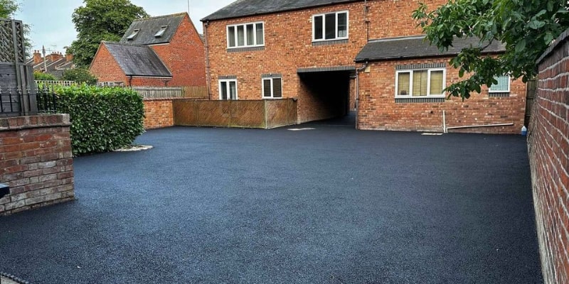 The image shows a large driveway that looks professionally made. The surface is smooth and even, with a dark black colour and is paved with asphalt.