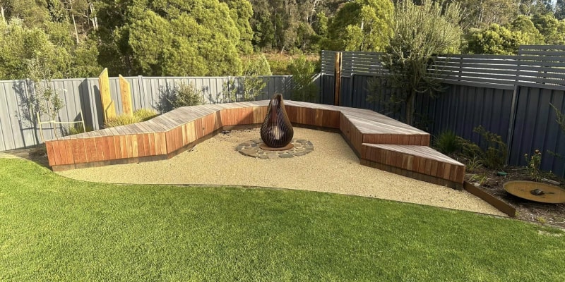 A neatly landscaped garden with professional metal and wood fencing, curved benches, and a central fire pit.